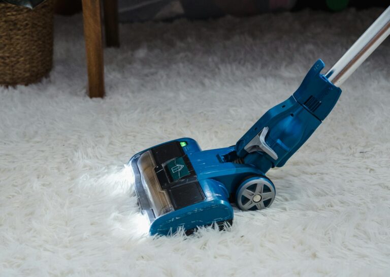 Modern blue vacuum cleaner on a white fur carpet in a cozy indoor setting.