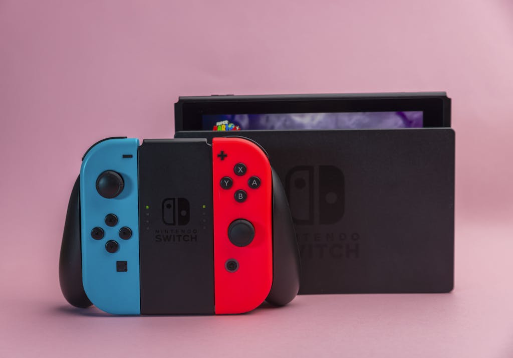 Close-up of Nintendo Switch console with red and blue Joy-Con controllers on pink background.