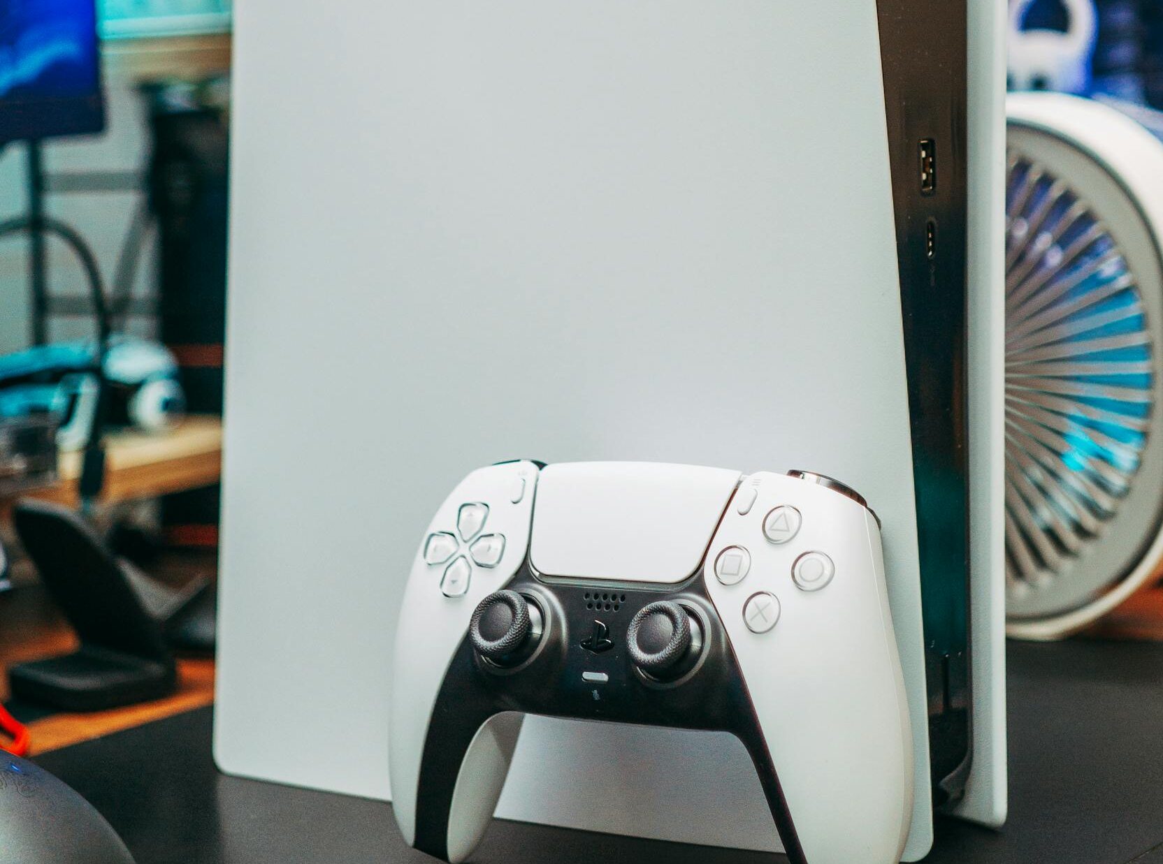 Close-up of PlayStation 5 and controller in an indoor gaming setup.