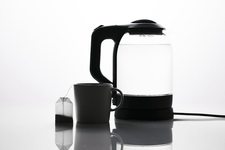 Minimalist image of a teabag beside a mug and electric kettle, emphasizing tea essentials.