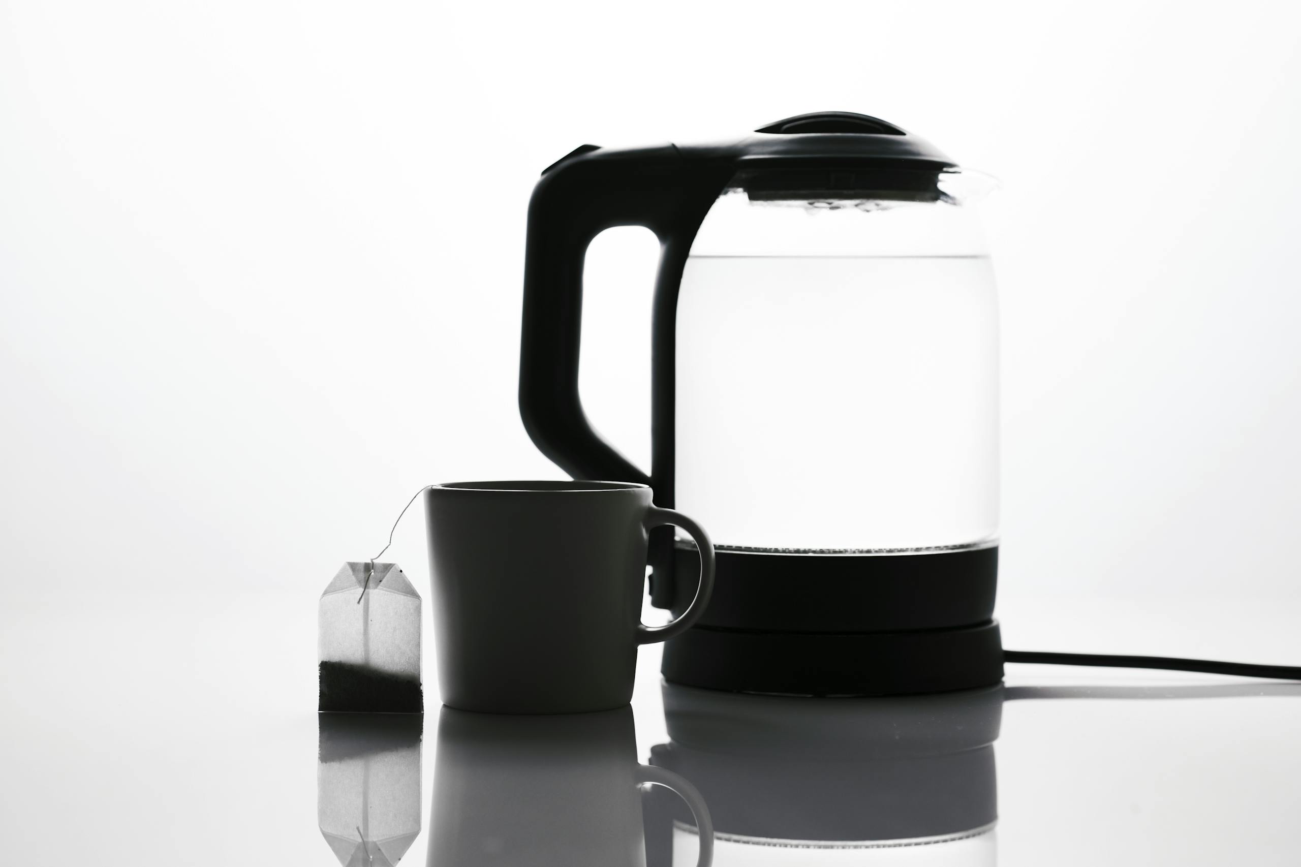 Minimalist image of a teabag beside a mug and electric kettle, emphasizing tea essentials.